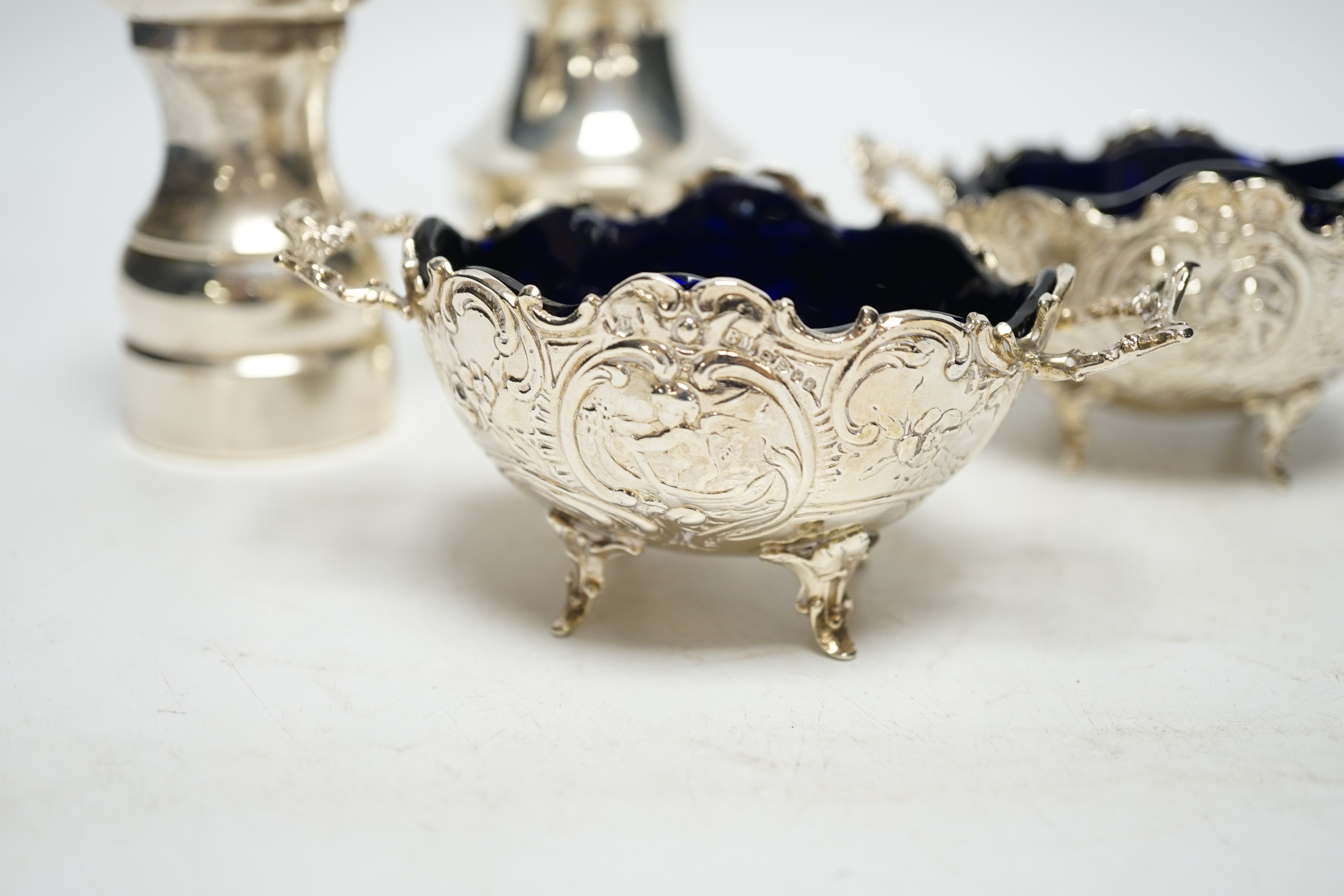 A pair of late 19th century Hanau silver two handled salts, with blue glass liners, import marks for Chester, 1899, with two associated spoons and two silver pepper mills. Condition - fair